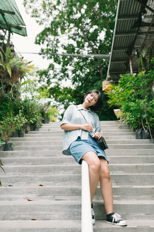 A Woman in a Gray Shirt and Denim Shorts Sitting on a Handrail