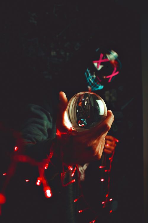 Free A masked person holding a glass ball with red lights, creating a mysterious atmosphere. Stock Photo