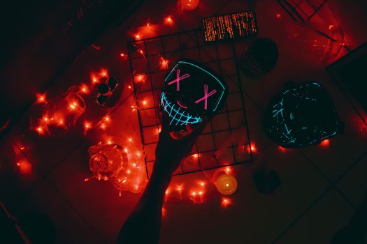 Flat lay of a neon mask surrounded by red lights, creating a vivid party atmosphere.