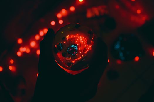 A hand holds a glowing orb with reflections, surrounded by red lights in a dark setting.