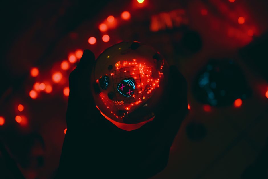 A hand holds a glowing orb with reflections, surrounded by red lights in a dark setting.