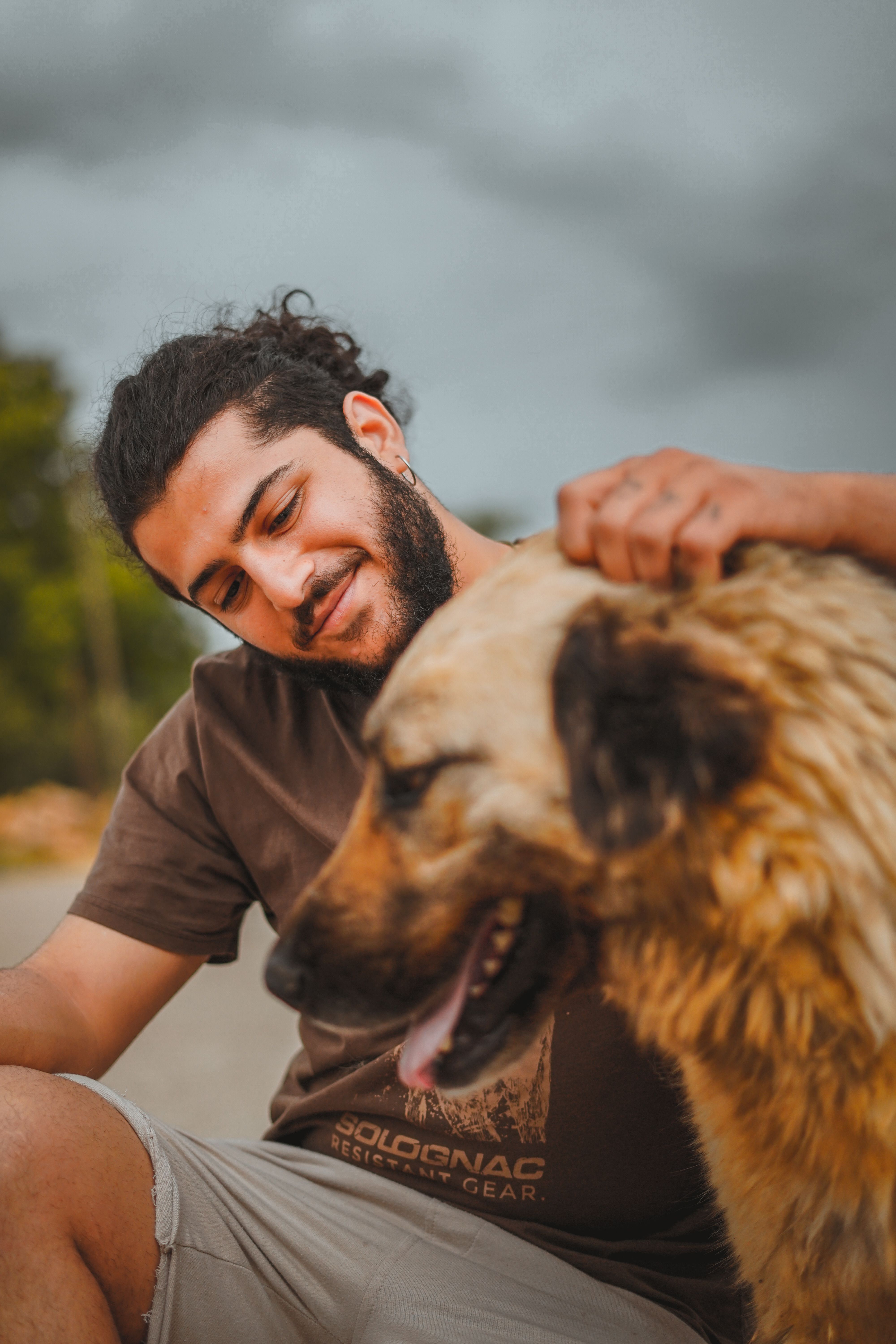 A man in a brown shirt smiling while petting a fluffy dog outdoors, showcasing companionship.