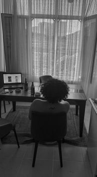 Monochrome image of a person seated, gazing out through a large window, in a serene setting.