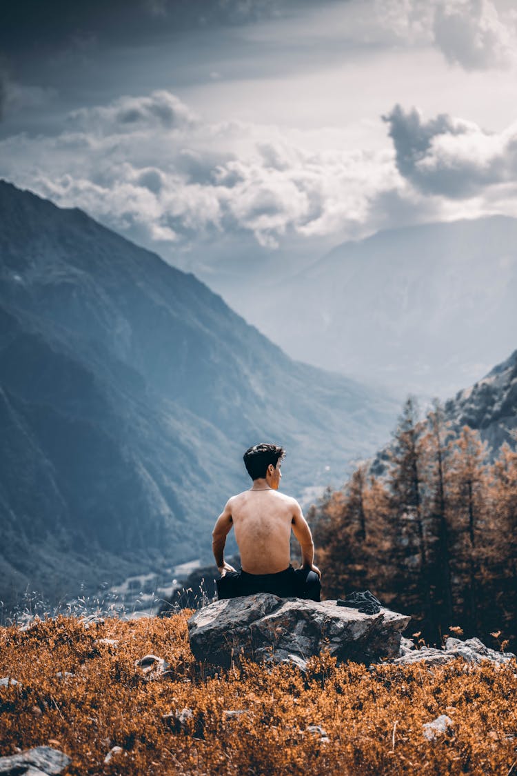 Shirtless Man Sitting On Mountain Peak