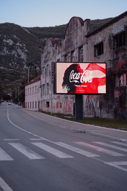 A Coca-Cola advertisement displayed on a billboard by an old building in a deserted street.