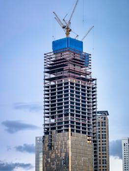 A contemporary skyscraper framed by cranes reaching the final stages of construction.