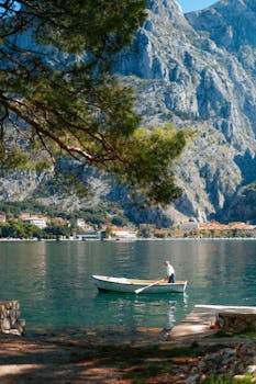 A man rows a boat on a serene lake surrounded by majestic mountains on a sunny day, offering a tranquil view.