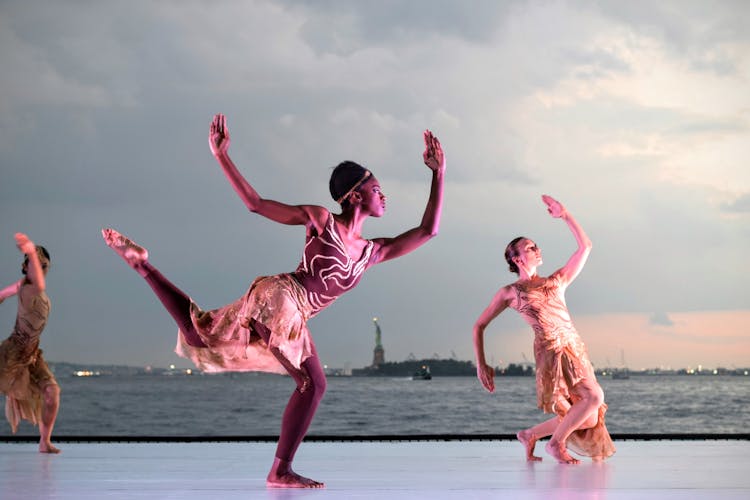 Three Women Dancing Near Body Of Water