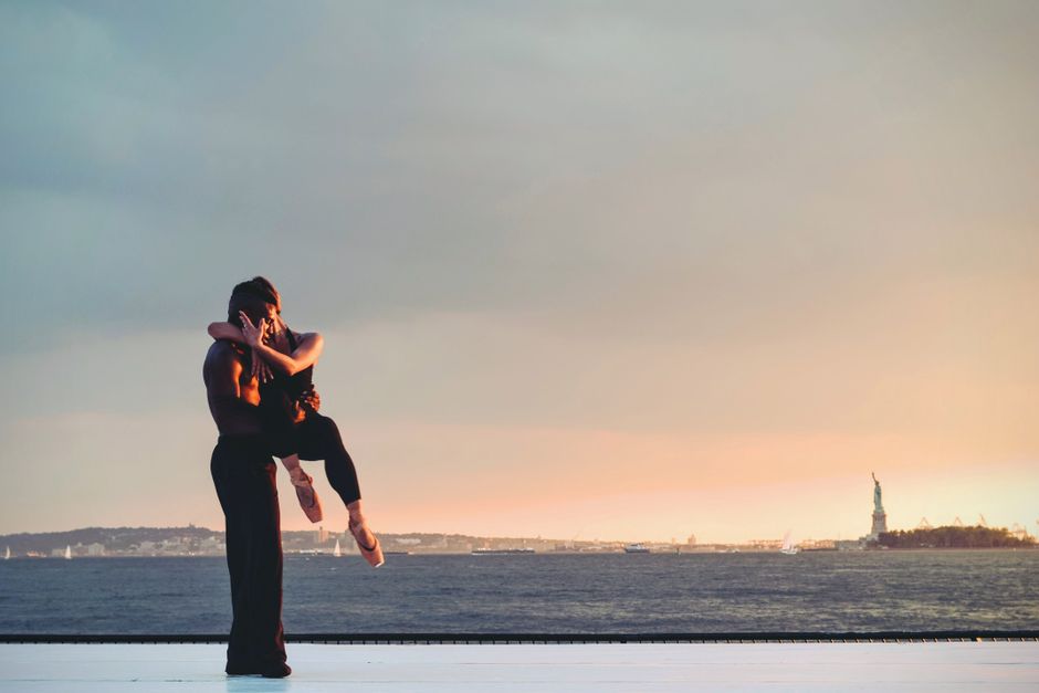 A couple performs a romantic dance by the Statue of Liberty with a stunning sunset backdrop.