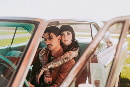 A young couple with tattoos embracing inside a vintage car, evoking a sense of romance and nostalgia.