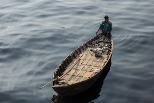 Free A man sits in a wooden boat floating on calm water, seen from above. Stock Photo