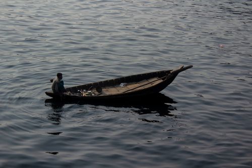 Free A man navigates a wooden boat on a tranquil lake, reflecting serene surroundings. Stock Photo