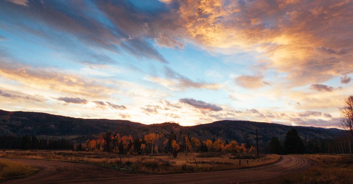 Beautiful sunset over a rural landscape in Steamboat Springs, Colorado with a winding dirt road and autumn foliage.