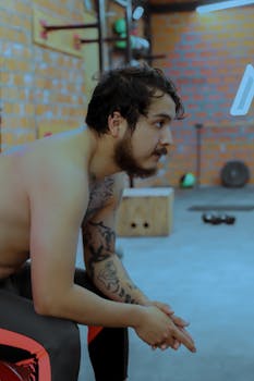 Focused man with tattoos rests in Mexico City gym, showcasing fitness and determination indoors.