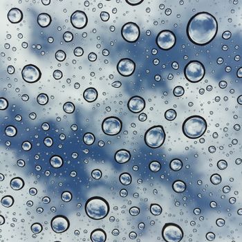 Artistic photo of raindrops on glass with sky and clouds reflecting, creating a captivating abstract pattern.
