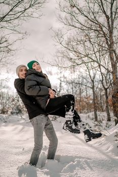 Man in Black Jacket and Gray Pants Carrying Girl in Black Jacket on Snow Covered Ground