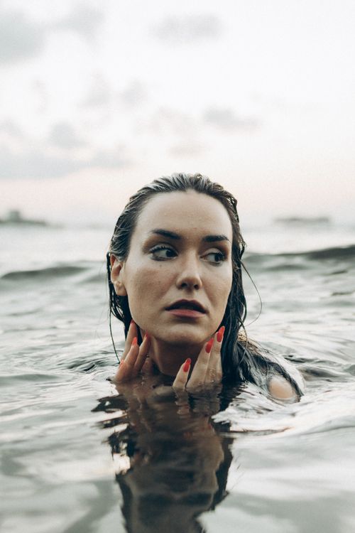 Free A contemplative woman with red nails in the ocean at dusk, showing beauty and calm. Stock Photo