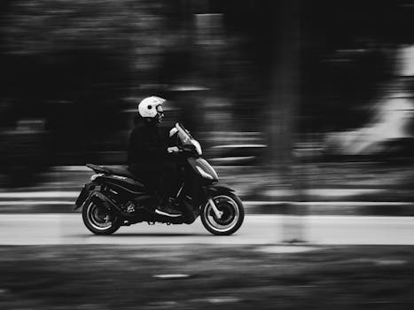 A person riding a scooter captured in motion blur with a monochrome effect, conveying speed and movement.