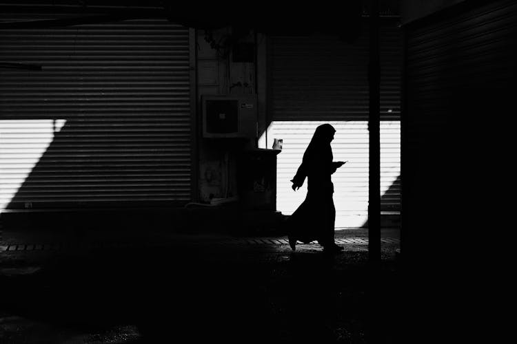 Silhouette Of Nun Walking Down Shady Street