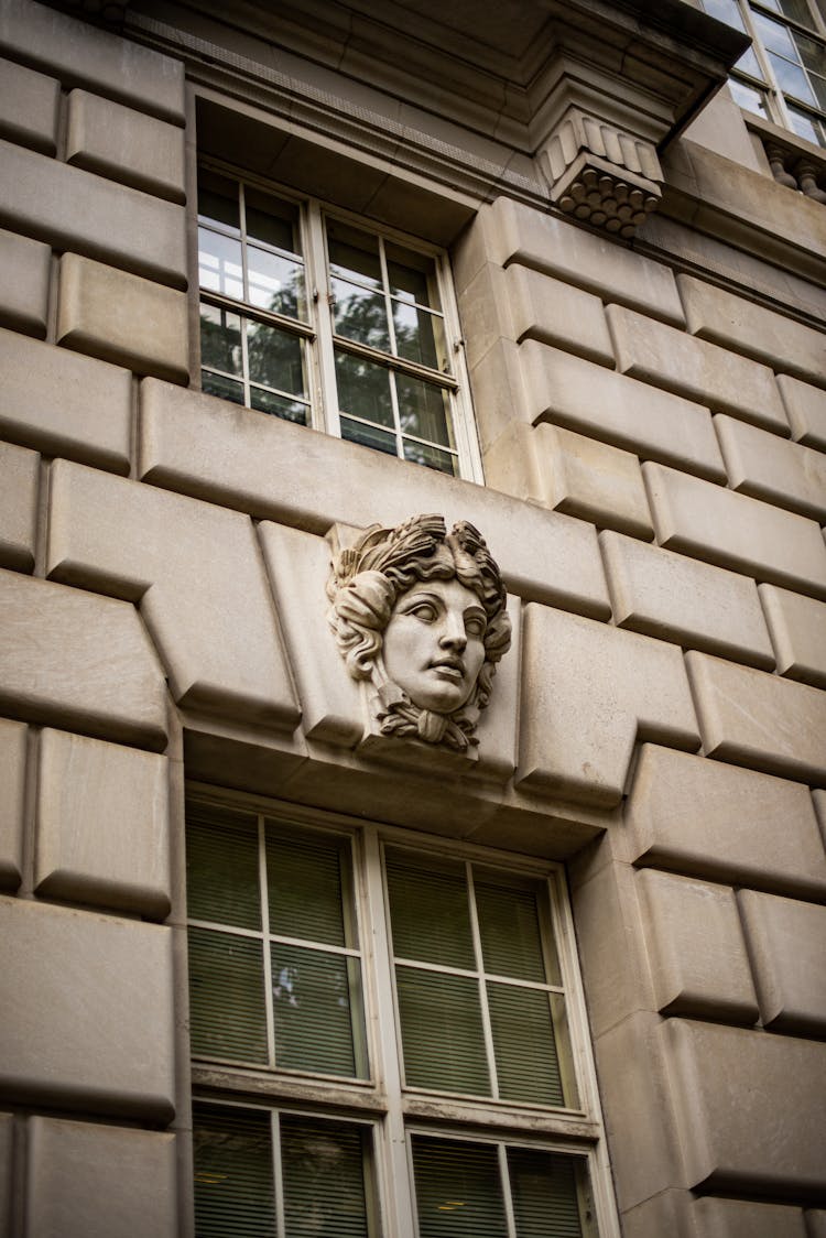 A Head Sculpture On A Wall Between Windows