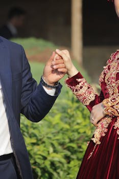 Close-up of a couple holding hands outdoors, showcasing elegant wedding attire.