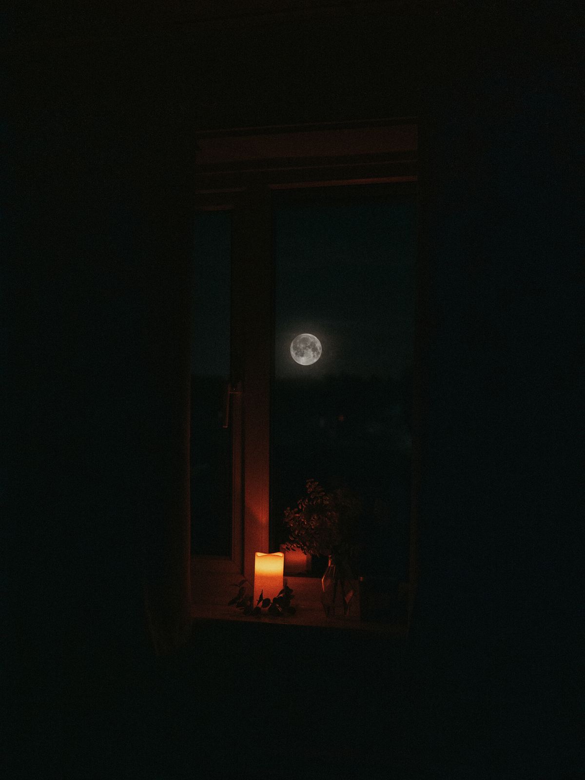 The moon seen through a window at night, with soft candlelight in the room