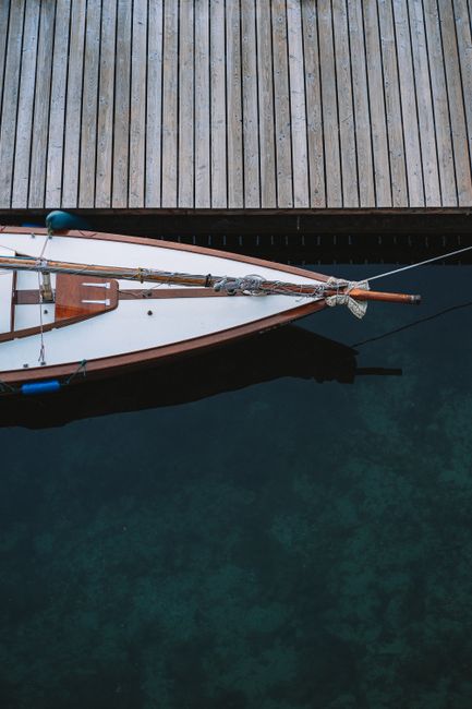 Aerial shot of a wooden boat docked beside a pier on clear waters.