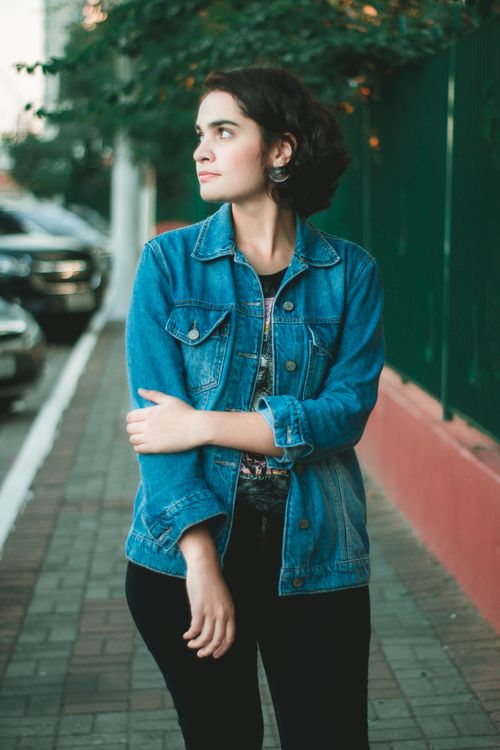 Free A young woman in a denim jacket poses confidently on a city sidewalk in Poá, Brazil. Stock Photo
