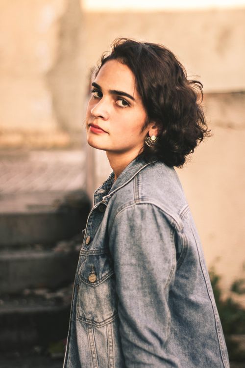 Free Young woman in a denim jacket gazing thoughtfully to the side outdoors. Stock Photo