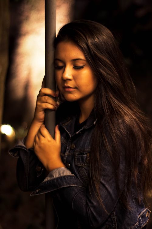 Free A serene woman in a denim jacket holding a pole during a night scene. Stock Photo