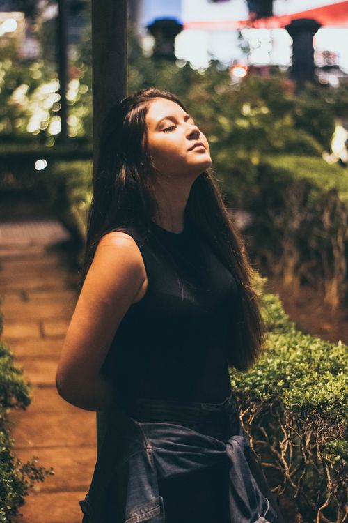 Free Woman in a tank top enjoying a calm night outdoors, eyes closed in relaxation. Stock Photo
