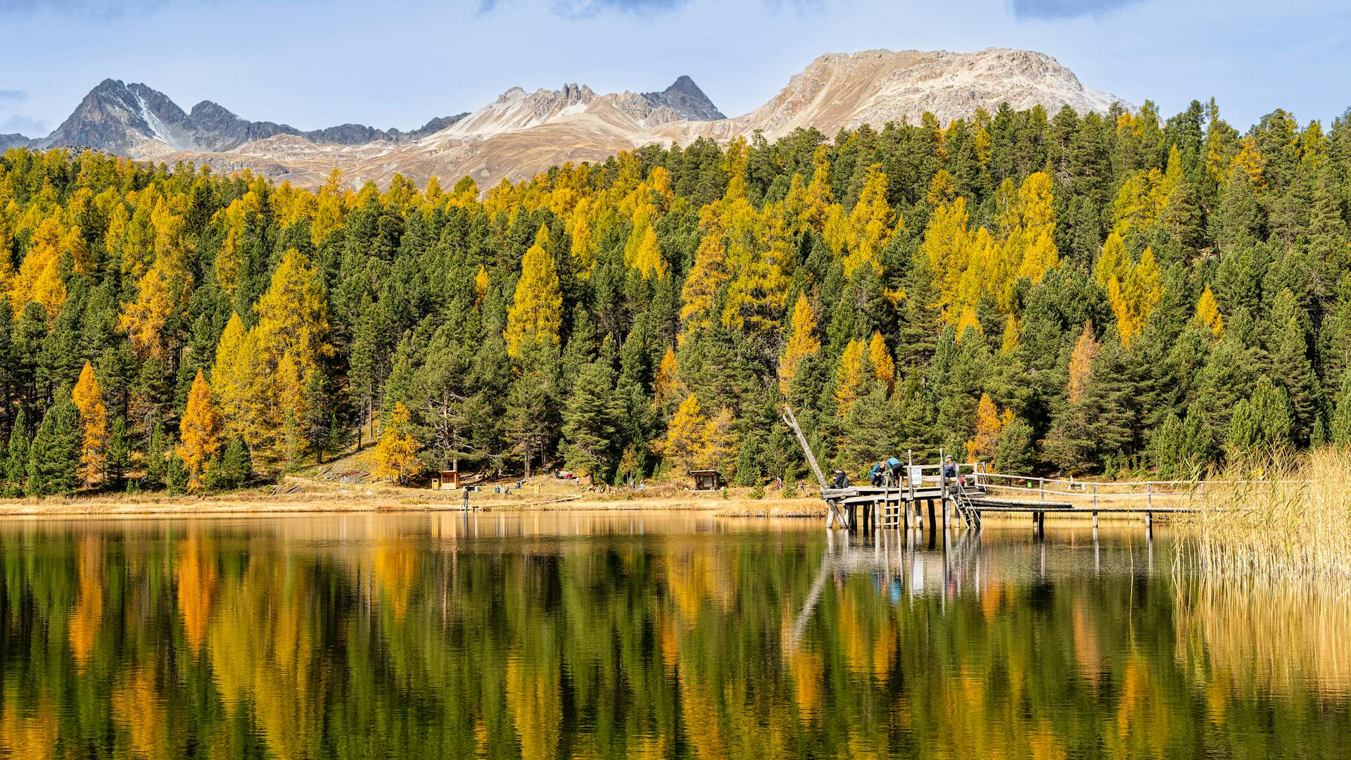 Serene autumn landscape of Lake St. Moritz with colorful trees and mountain backdrop.