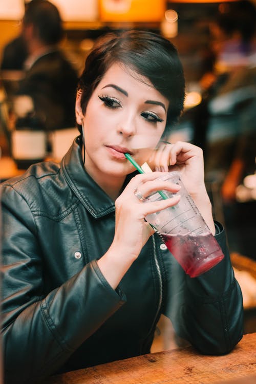 Woman in Black Leather Jacket Looking Sideways and Drinking Cold Beverage