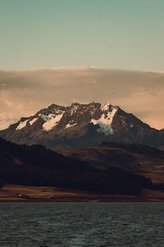 Stunning view of a snow-capped mountain in the Andes at sunrise, with a serene lake in the foreground.