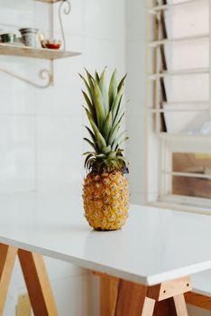 A fresh pineapple placed on a modern white table by a kitchen window, capturing simplicity and freshness.