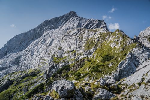 Free A breathtaking view of a rocky mountain peak with clear blue skies and lush green grass. Stock Photo