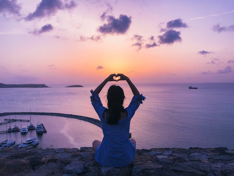 Woman Sitting On Rock Doing Heart Hand Gesture