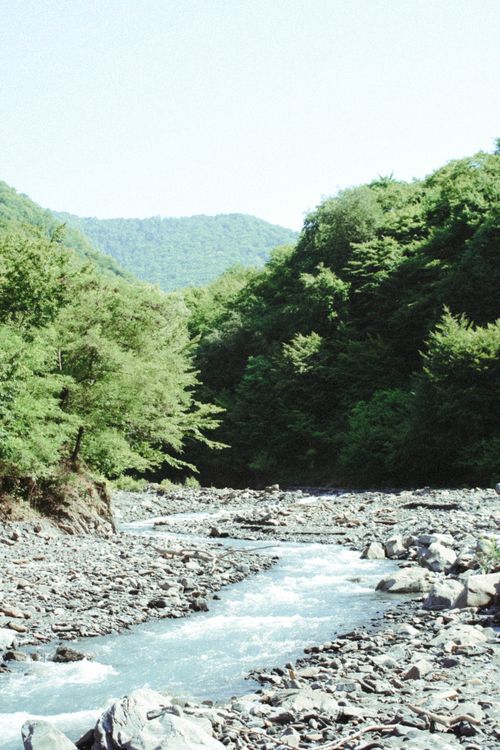 Free Tranquil river winding through rocky landscape surrounded by verdant mountains and trees. Stock Photo