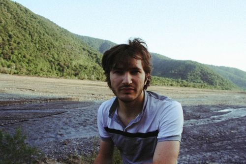 Free A young man enjoying nature with lush hills and a rocky riverbed in the background. Stock Photo
