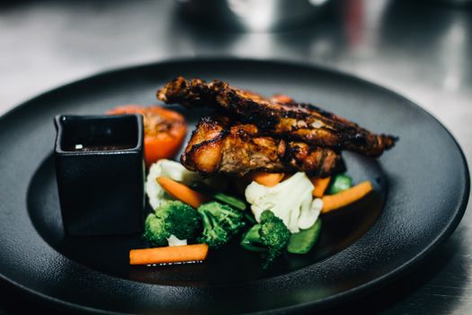 Grilled chicken served with fresh vegetables on a black plate.