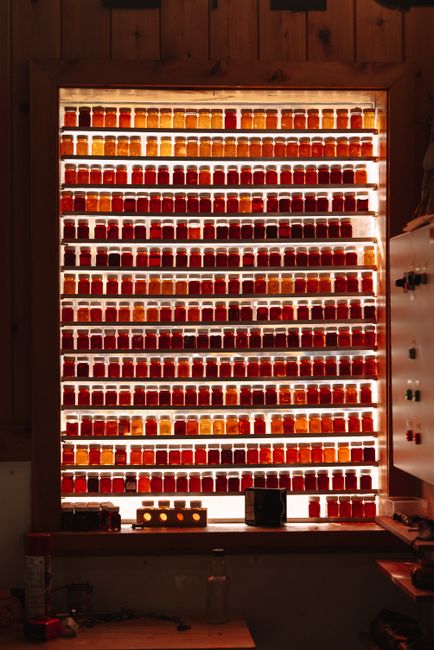 A collection of illuminated jars filled with assorted colored maple syrup displayed on shelves in a vertical shot.