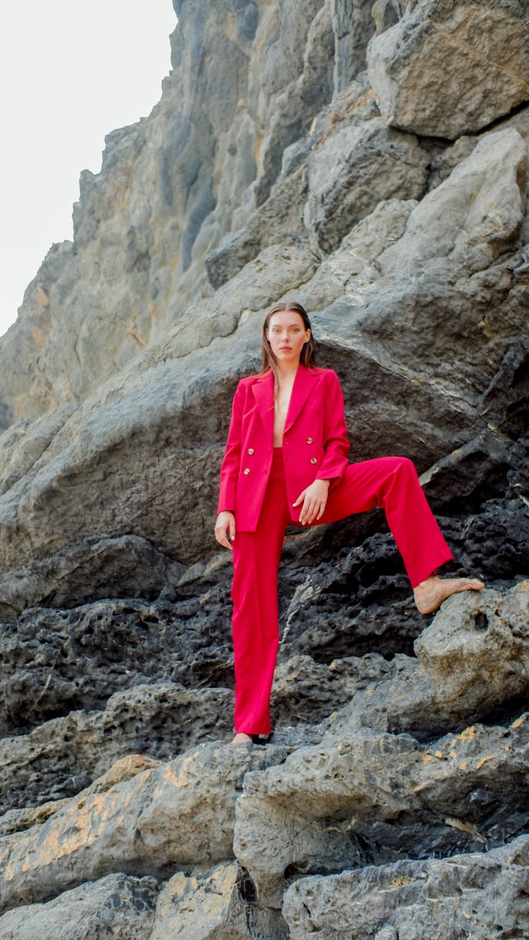 Woman Standing Barefoot On A Rock Wearing Red Trouser Suit