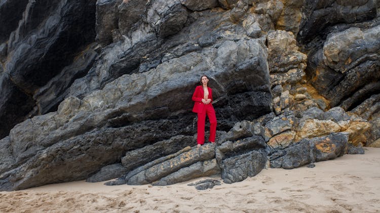 A Woman In Red Suit Standing On Rocks
