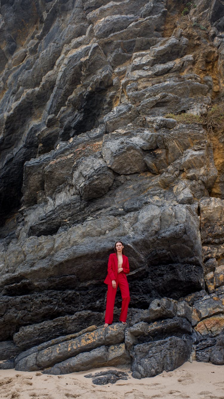 A Woman In Red Suit Standing On Rocks
