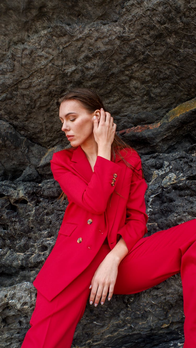 A Woman In Red Suit Jacket Sitting On Rocks
