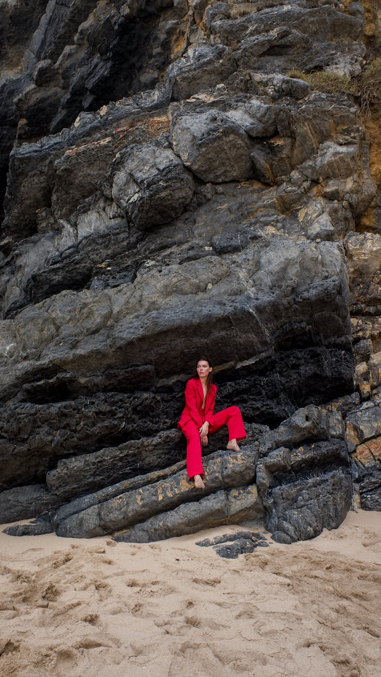 A Woman In Red Suit Sitting On Rocks
