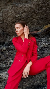 A stylish woman sits on rocks wearing a vibrant red suit, showcasing modern fashion.