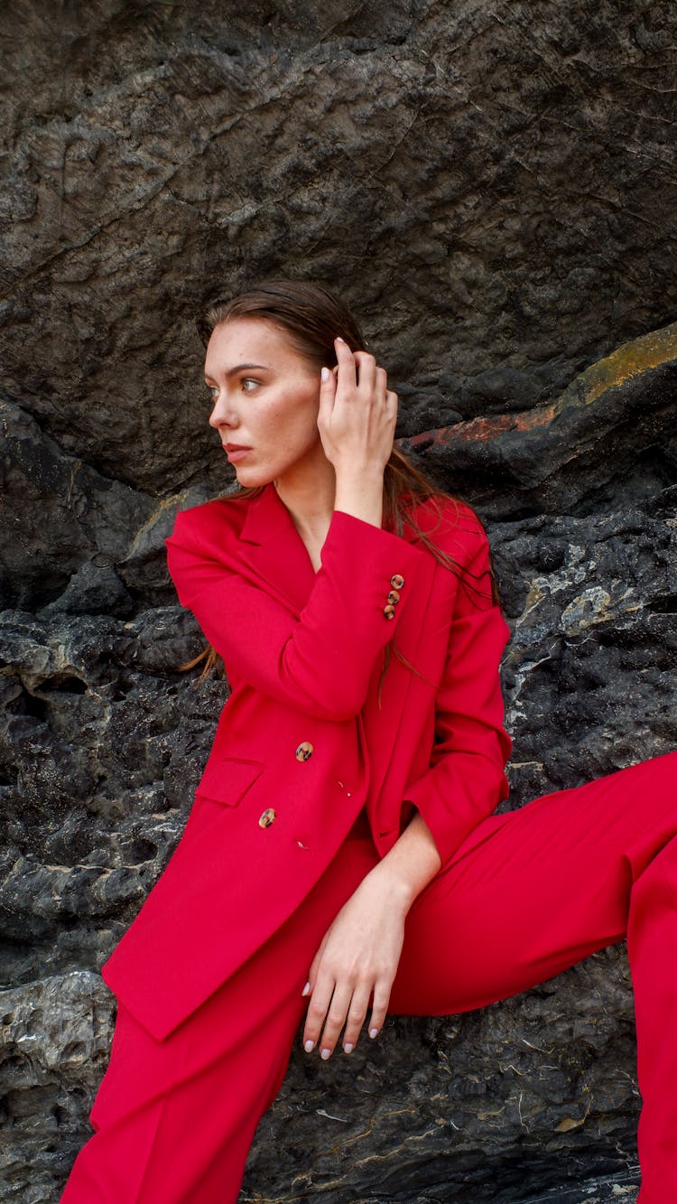 A Woman In Red Suit Jacket Sitting On Rocks
