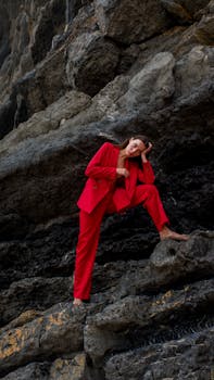Elegant woman wearing red suit poses confidently against dramatic rock formations.