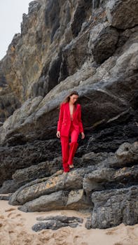Stylish woman in red suit posing on a rocky beach outdoors.